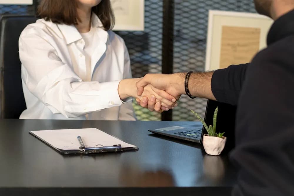 Man and woman shaking hands in front of a laptop in a professional setting